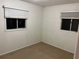 Carpeted spare room featuring a textured ceiling and baseboards