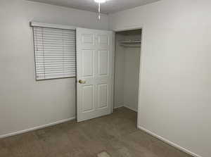 Unfurnished bedroom featuring a textured ceiling, carpet flooring, and a closet