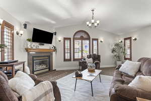 Carpeted living area featuring vaulted ceiling, a glass covered fireplace, and a chandelier