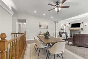 Dining space with vaulted ceiling, a glass covered fireplace, recessed lighting, light colored carpet, and ceiling fan