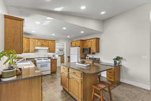 Kitchen featuring a center island, white appliances, dark stone counters, recessed lighting, and brown cabinets