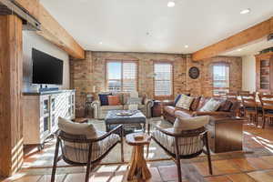 Living room featuring brick wall, beam ceiling, plenty of natural light, and recessed lighting