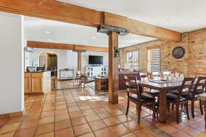 Dining room with brick wall, beamed ceiling, arched walkways, and light tile patterned floors