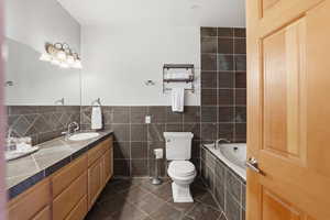 Full bathroom with tile walls, vanity, and dark tile patterned flooring