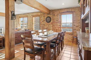 Dining room with brick wall, beam ceiling, recessed lighting, and light tile patterned floors