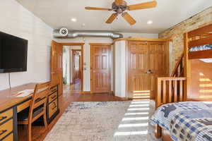 Bedroom with brick wall, an office area, hardwood / wood-style floors, and ceiling fan