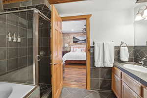 Ensuite bathroom with vanity, dark tile patterned floors, a shower stall, and a tub