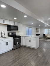 Kitchen with stainless steel appliances, white cabinetry, a peninsula, dark wood-style flooring, and recessed lighting