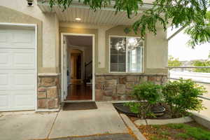 Doorway to property with stone siding, stucco siding, and a garage