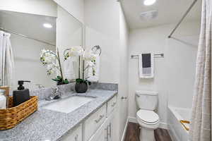 Bathroom featuring vanity, shower / tub combo with curtain, and dark wood-type flooring