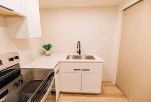 Kitchen featuring stainless steel range with electric cooktop, white cabinetry, light wood-type flooring, and custom exhaust hood