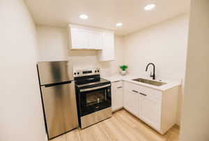 Kitchen featuring appliances with stainless steel finishes, white cabinets, recessed lighting, light wood-style flooring, and light stone countertops