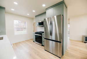 Kitchen with appliances with stainless steel finishes, green cabinets, recessed lighting, light wood-type flooring, and light countertops