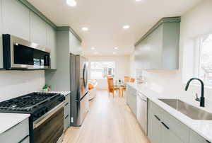 Kitchen with green cabinetry, stainless steel appliances, recessed lighting, and light wood-style floors