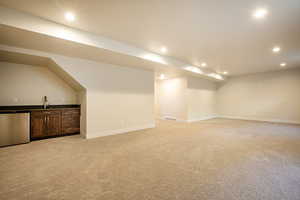 Finished basement with light carpet, recessed lighting, and bar with sink
