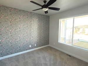 Carpeted spare room featuring wallpapered walls, a textured ceiling, a ceiling fan, and an accent wall
