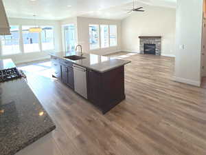 Kitchen featuring dark stone counters, dark brown cabinetry, open floor plan, a kitchen island with sink, and a fireplace
