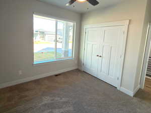 Unfurnished bedroom featuring a closet, a ceiling fan, and dark colored carpet