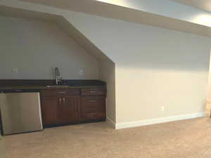 Bar area with dark brown cabinets, dishwasher, dark countertops, lofted ceiling, and light colored carpet