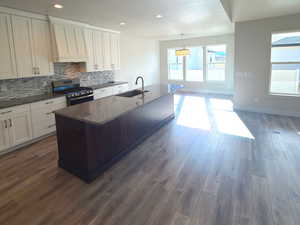 Kitchen with a center island with sink, white cabinetry, dark stone countertops, gas stove, and premium range hood