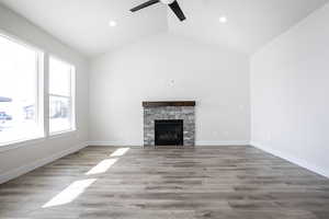 Unfurnished living room featuring light wood-style floors, a stone fireplace, lofted ceiling, a ceiling fan, and recessed lighting