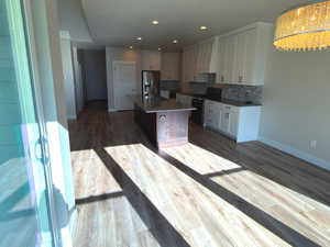 Kitchen with white cabinetry, a center island with sink, dark wood finished floors, stainless steel appliances, and backsplash
