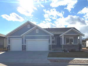 View of front of house featuring driveway, a garage, stone siding, and covered porch