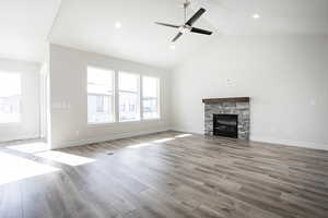 Unfurnished living room with light wood-type flooring, a stone fireplace, a ceiling fan, recessed lighting, and high vaulted ceiling