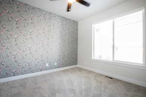 Empty room with wallpapered walls, carpet floors, a ceiling fan, and an accent wall