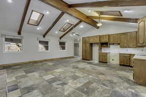 Kitchen with light countertops, a skylight, stone tile floors, tasteful backsplash, and beam ceiling