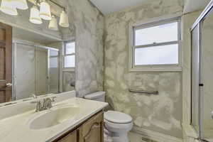 Bathroom featuring a marble finish shower, vanity, and wallpapered walls
