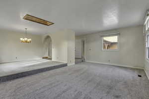 Unfurnished living room featuring arched walkways, carpet flooring, and a chandelier