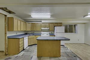 Kitchen featuring white appliances, dark countertops, a center island, and light brown cabinets