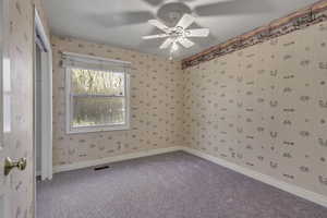 Spare room featuring wallpapered walls, ceiling fan, and carpet floors