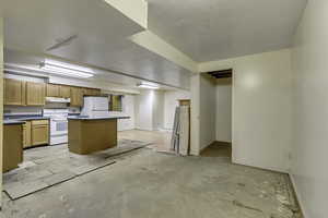 Kitchen with white appliances, a center island, dark countertops, under cabinet range hood, and unfinished concrete floors