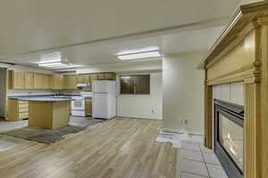 Kitchen featuring white appliances, light wood-style floors, a center island, light countertops, and a tile fireplace