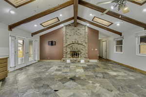 Unfurnished living room with a skylight, french doors, stone tile floors, a fireplace, and ceiling fan