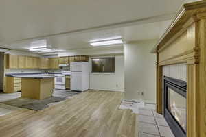 Kitchen with white appliances, light wood-style flooring, a fireplace, light countertops, and a center island