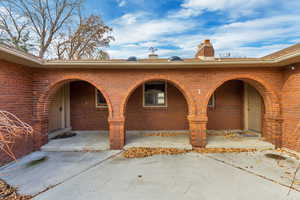 View of exterior entry featuring brick siding, a chimney, and covered porch