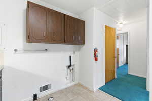 Washroom featuring light carpet, cabinet space, gas dryer hookup, and light tile patterned floors