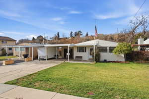 View of front of home with a front lawn, driveway, an attached carport, and a patio