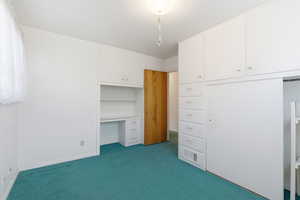 Unfurnished bedroom with dark colored carpet and built in desk