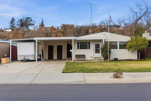 View of front of house featuring an attached carport, a front lawn, concrete driveway, entry steps, and a chimney