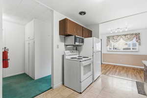 Kitchen featuring white electric range oven, stainless steel microwave, light countertops, and light tile patterned floors