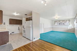 Kitchen featuring light countertops, white appliances, light wood finished floors, dark brown cabinets, and light carpet