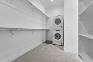 Washroom with stacked washer / drying machine and light colored carpet