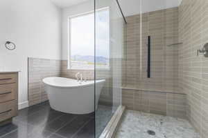 Full bath featuring vanity, a freestanding bath, tile walls, tiled shower, and dark tile patterned floors