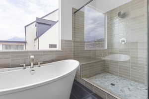 Bathroom with a tile shower, a freestanding bath, and tile walls