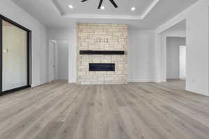 Unfurnished living room with a stone fireplace, ceiling fan, light wood-style floors, and recessed lighting