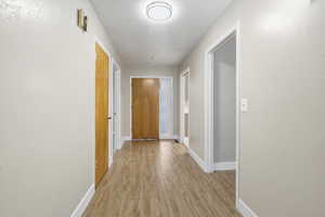 Corridor with light wood-style floors, a textured ceiling, and a textured wall
